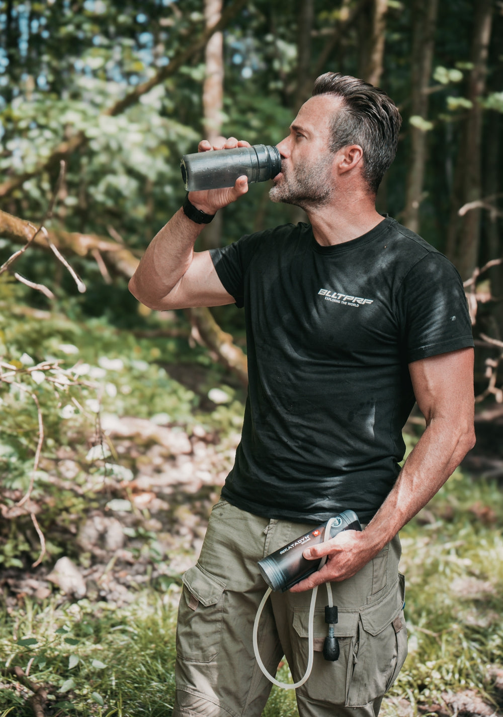 Man drinking filtered water from a Katadyn Explorer water filter in a forest.